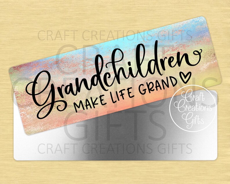 Puede incluir: Un letrero rectangular con un fondo de acuarela pastel y las palabras "Grandchildren Make Life Grand" en escritura negra. Un s&iacute;mbolo de coraz&oacute;n est&aacute; al lado de la palabra "Grand". El letrero est&aacute; sobre un rect&aacute;ngulo plateado.