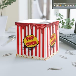 May include: A square popcorn-themed notepad with red and white stripes, a dripping red top, and the words "POP CORN" in a yellow cloud. The base of the notepad is lined with popcorn kernels.