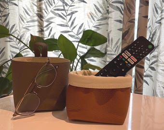 May include: Two small, brown leather containers with white fabric lining. One container holds a pair of eyeglasses, and the other holds a black remote control.