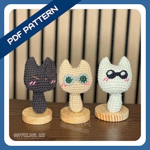 May include: Three crocheted cat figures in black, beige, and white, each with unique facial expressions and details. The black cat has a grumpy face, the beige cat wears green glasses, and the white cat has black sunglasses. Each cat sits on a wooden base. The text "PDF PATTERN" is in the upper left corner.