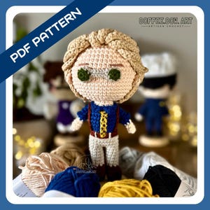 May include: Crochet amigurumi doll pattern for a character with blonde hair, wearing a blue shirt, brown pants, and a red vest. The doll is sitting on a table with yarn balls in the background. The text "COFFEE.COW.ART - ARTISAN CROCHET" is visible in the top right corner of the image.