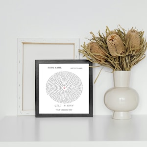May include: A black framed print with a white background featuring a circular design of song lyrics in a spiral pattern. The center of the spiral has a red heart with the number 9 inside. Below the spiral, the text reads "Gill & Ron" and "Your message here".