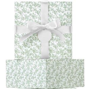 May include: A wrapped gift box with a white satin ribbon and bow. The gift wrap has a floral pattern in shades of green and white. A blank, round tag hangs from the bow.