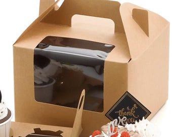 May include: A brown cardboard bakery box with a clear window and a handle. The box is partially open, revealing a cupcake inside. A black sticker with gold text that says "thank you" is on the box.
