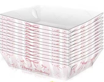 May include: A stack of white and pink paper trays with a bow and stripe design. The words "Happy Birthday" are printed on the front of the trays. These trays are perfect for serving food at a birthday party.