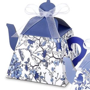 May include: A blue and white teapot-shaped gift box with a floral design. The box features a white ribbon and a blue handle and spout. The floral pattern includes blue flowers, butterflies, and branches.