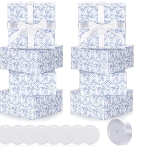 May include: Gift boxes in various sizes, wrapped in white paper with a blue floral pattern. Each box is tied with a white ribbon and bow. Includes white gift tags and a roll of white ribbon, perfect for wrapping presents.