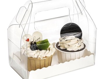 May include: A clear plastic cupcake carrier holding two cupcakes. One cupcake has white frosting, blueberries, and kiwi. The other has white frosting and an Oreo cookie. A white heart with the word "Love" is visible.