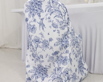 May include: A white chair cover with a blue floral pattern. The cover is draped over a chair, showcasing a classic toile design. The floral print includes various flowers and foliage, creating an elegant look.