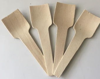 May include: Four wooden disposable spoons with a light brown color. Each spoon has a flat, rectangular head and a long, narrow handle. The spoons are arranged in a fan shape, with the handles pointing towards the center.