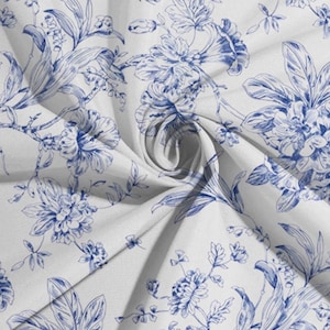 May include: White fabric with a blue floral pattern. The design features detailed illustrations of flowers, leaves, and vines. The fabric is folded, creating shadows and depth, highlighting the intricate pattern.
