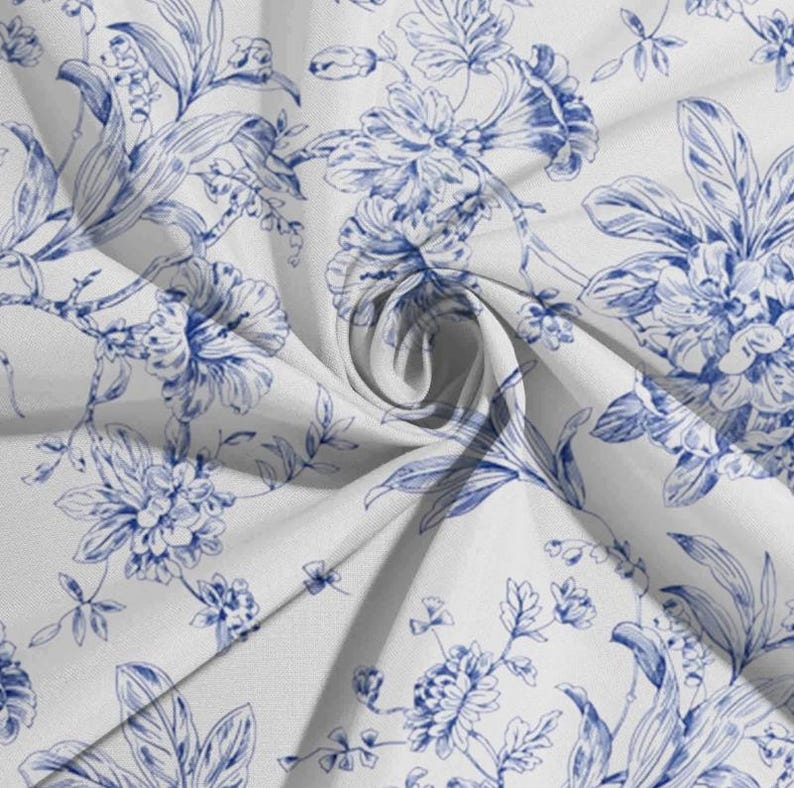May include: White fabric with a blue floral pattern. The design features detailed illustrations of flowers, leaves, and vines. The fabric is folded, creating shadows and depth, highlighting the intricate pattern.