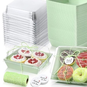 May include: A collection of bakery boxes with clear lids, stacked and filled with treats. The boxes are light green and tied with green twine. The treats include cupcakes and donuts, with "Handmade with love" tags.