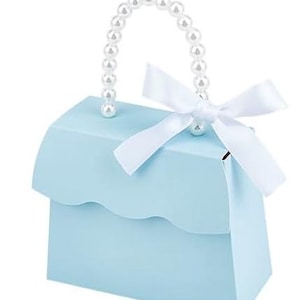 May include: A light blue gift box shaped like a purse, featuring a scalloped edge and a handle made of white pearls. A white satin bow adorns the top. The box is designed for small gifts or favors.