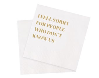 May include: White paper napkins with gold text reading "I FEEL SORRY FOR PEOPLE WHO DON'T KNOW US." The napkins are folded and stacked, suitable for a party or event.