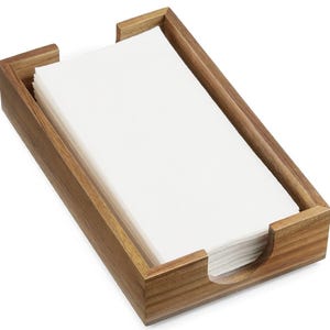 May include: A rectangular wooden napkin holder with a stack of white napkins. The holder is made of light brown wood and has a simple, modern design. The napkins are neatly stacked inside the holder, ready for use.