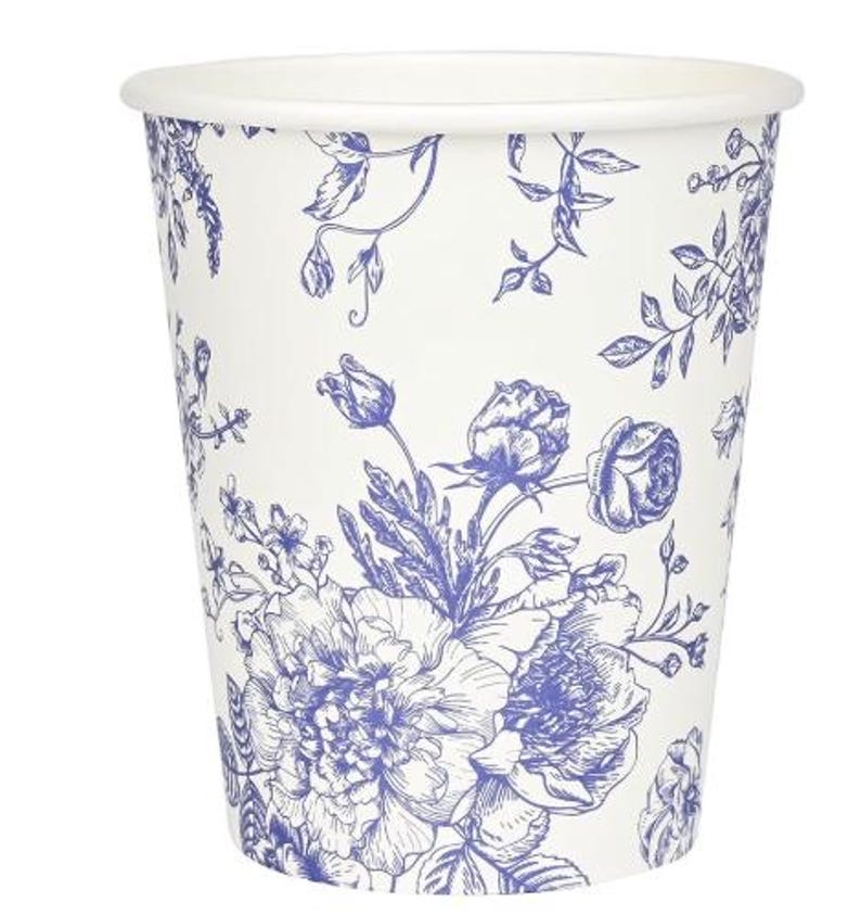 Op de afbeelding: Een witte papieren beker met een blauw bloemmotief. Het ontwerp bevat gedetailleerde illustraties van rozen, pioenrozen en andere bloemen en bladeren. De beker heeft een eenvoudig ontwerp met een gerolde rand.