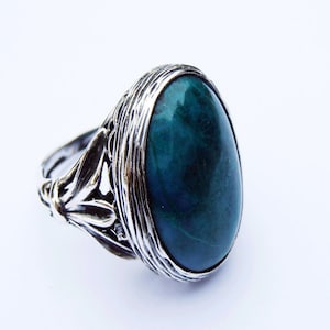May include: A silver ring with a large oval green gemstone set in a detailed filigree design.