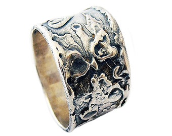 Puede incluir: Un anillo ancho de plata con un diseño intrincado y texturizado. El anillo tiene un acabado martillado y un aspecto ligeramente oxidado.
