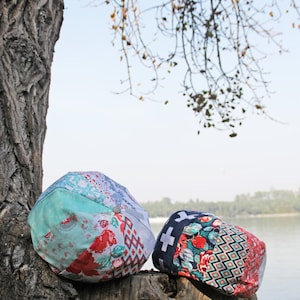 Könnte beinhalten: Zwei Stoff-Patchwork-Eimerhüte, einer in Blautönen, Grün und Rot, der andere in Rot-, Grün- und Schwarztönen, die auf einem Baumstamm liegen.