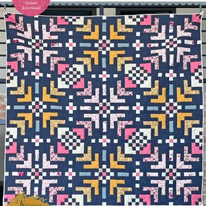 Könnte beinhalten: Eine marineblaue Steppdecke mit einem Schneeflockenmuster. Die Steppdecke zeigt geometrische Formen in Rosa, Gelb, Weiß und Blau. Der Text "SNOWFLAKE MAGIC quilt pattern" steht oben. Die Größen sind Lap 135cm sq., Twin 135cm x 203cm, Bed 203cm sq., Full 203cm x 272cm, und King 272cm sq.