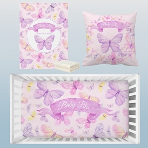 May include: A baby bedding set featuring a pink background with watercolor butterflies in shades of purple, pink, and yellow. The set includes a crib sheet, a pillow, and a blanket, each with the name "Baby Lila" on a banner.