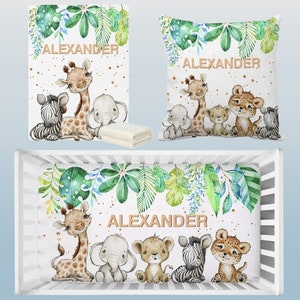 May include: A white crib bedding set with a jungle theme. The set includes a fitted sheet, a crib bumper, and a pillow. The bedding features a green and blue leafy pattern with gold glitter accents. The crib bumper has a row of adorable jungle animals including a giraffe, elephant, lion, zebra, and leopard. The pillow has the name "ALEXANDER" written in gold letters.