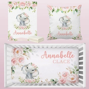 May include: A pink and green floral crib bedding set with a cute elephant design. The bedding set includes a fitted sheet, a crib blanket, and a pillow. The set is personalized with the name "Annabelle Claice".