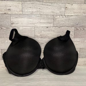 May include: A black underwire bra with molded cups and a subtle shimmering texture. The garment features adjustable shoulder straps and a central bridge connecting the two cups, providing a structured silhouette with a smooth, uniform finish.
