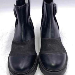 May include: A pair of black ankle boots featuring a smooth leather upper, a suede-textured mid-section, and a rounded toe cap. Each boot includes a side buckle strap detail, a pull tab at the heel, and a thick, lugged rubber sole for traction.