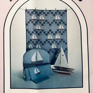 May include: A quilt pattern titled "Sails" by Great American Quilt Factory, Inc. The pattern features a blue and white checked background with white sailboats. The image also shows a blue and white sailboat cushion and a toy sailboat.