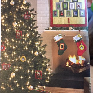 Könnte beinhalten: Ein grüner Weihnachtsbaum, der mit Ornamenten und gerahmten Fotos geschmückt ist. Der Baum ist mit weißen Lichtern geschmückt und hat einen grünen Baumrock mit rotem und weißem Besatz. Es gibt einen Kamin mit Strümpfen, die am Kaminsims hängen, und eine Steppdecke mit einem Weihnachtsbaumdesign, die an der Wand hängt.