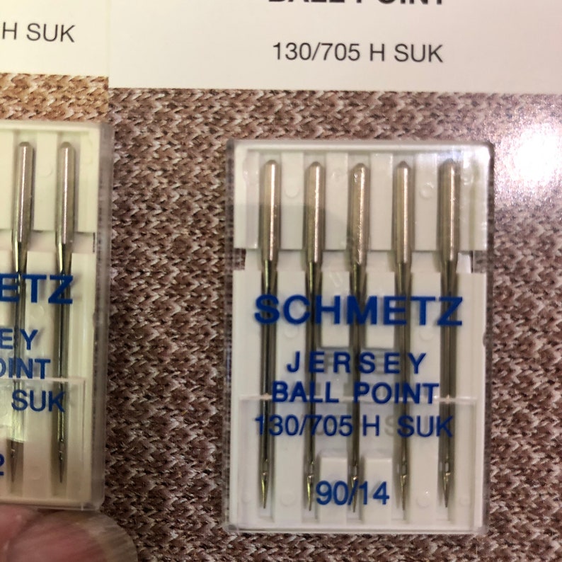May include: A pack of four silver sewing needles labeled "Schmetz Jersey Ball Point 130/705 H SUK 90/14".