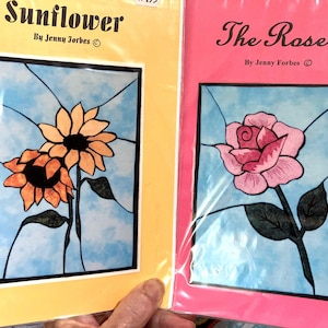 May include: Two stained glass patterns, one of a sunflower and one of a rose. The sunflower pattern is on a yellow background and the rose pattern is on a pink background. Both patterns have the text "By Jenny Forbes" and a copyright symbol.