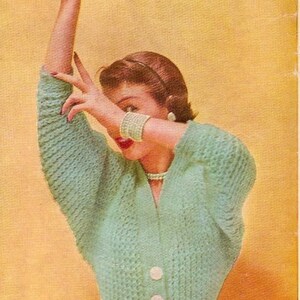 May include: A teal knitted cardigan with a V-neck and four white buttons. The cardigan is worn by a person with their arm raised, covering their face.