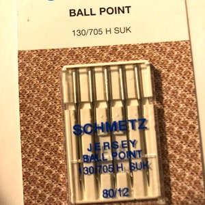 May include: A pack of six silver ball point sewing needles for jersey fabric. The needles are labeled "Schmetz Jersey Ball Point 130/705 H SUK 80/12".