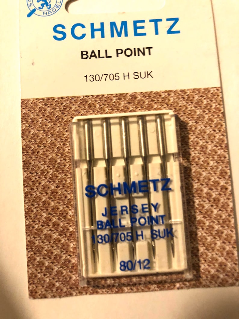May include: A pack of six silver ball point sewing needles for jersey fabric. The needles are labeled "Schmetz Jersey Ball Point 130/705 H SUK 80/12".