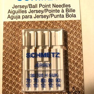 May include: A pack of five Schmetz Jersey/Ball Point needles for sewing. The needles are packaged in a clear plastic case with a white label that reads "Schmetz Jersey" and "130/705 H SUK". The label also lists the sizes of the needles: 70, 80, and 90. The pack is labeled "5 PC/PZ".