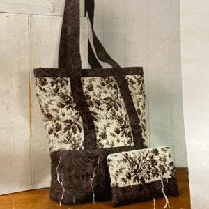May include: A tote bag and matching clutch set. The bag has a rectangular shape with long handles and a floral pattern on a cream background. The bottom and handles are a dark brown, patterned fabric. The clutch mirrors the bag's design.