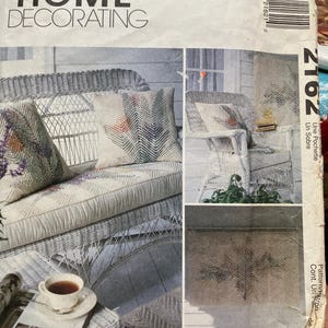 May include: A vintage McCall's Home Decorating pattern envelope. The cover shows images of wicker furniture with patterned cushions and a matching rug. The text "Faux Chenille" is visible. A cup of tea and a magazine are on a wicker table.