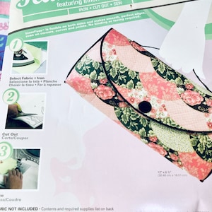 May include: A pink and green floral handbag kit featuring InnerFuse, a fusible fabric that makes smooth, perfect edges. The kit includes instructions for selecting fabric, cutting out the pattern, and sewing the handbag. The finished handbag measures 30.48 cm by 16.51 cm.