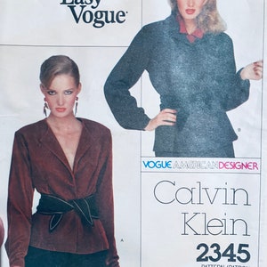 May include: A vintage sewing pattern for a blouse by Calvin Klein. The pattern is for Vogue American Designer pattern number 2345. The pattern features two models wearing different versions of the blouse. One model is wearing a dark brown blouse with a black belt, and the other model is wearing a dark gray blouse.