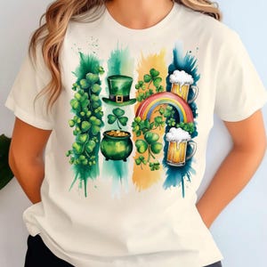 Puede incluir: Una camiseta blanca con un diseño de acuarela que presenta un trébol verde, una olla de oro, un sombrero de duende, un arcoíris y dos jarras de cerveza.
