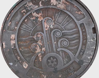 May include: A weathered, circular metal storm sewer cover with a stylized design. The design includes sun rays, waves, and floral elements. Text includes "Miami Beach Public Works", "Storm Sewer", and "Made in U.S.A."