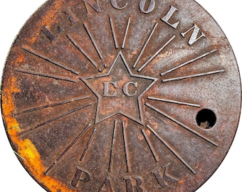 May include: A circular, rusty metal object with the words "LINCOLN PARK" embossed around the edge. A star with the letters "EC" in the center is surrounded by radiating lines. A small hole is visible near the edge.