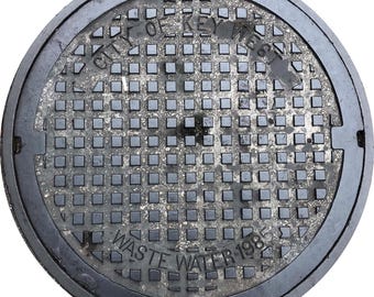 May include: A circular, weathered manhole cover with the text "CITY OF KEY WEST" and "WASTE WATER 1985". The cover has a grid of square indentations and a dark, metallic appearance.