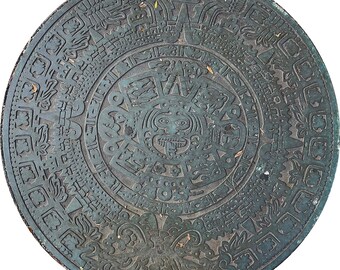 May include: A circular, bronze-colored Aztec calendar stone with intricate carvings. The central figure is a sun god with a protruding tongue, surrounded by detailed glyphs and symbols. The stone's surface has a weathered appearance.