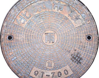May include: A circular, weathered metal manhole cover with a grid pattern and Chinese characters. The cover has two small holes and the text "QT-700". The design is centered with concentric circles and rectangular patterns.