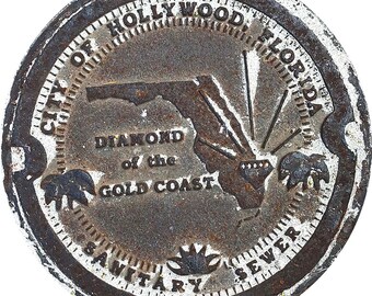 May include: A weathered, circular metal sewer cover from the City of Hollywood, Florida. The design includes the Florida outline, the words "DIAMOND of the GOLD COAST", and the text "SANITARY SEWER". The cover has a diamond and sunburst design.