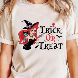 May include: A white t-shirt with a black and red graphic of a witch dressed as Ariel from The Little Mermaid. The graphic includes the text "Trick or Treat" with bats and a skull.